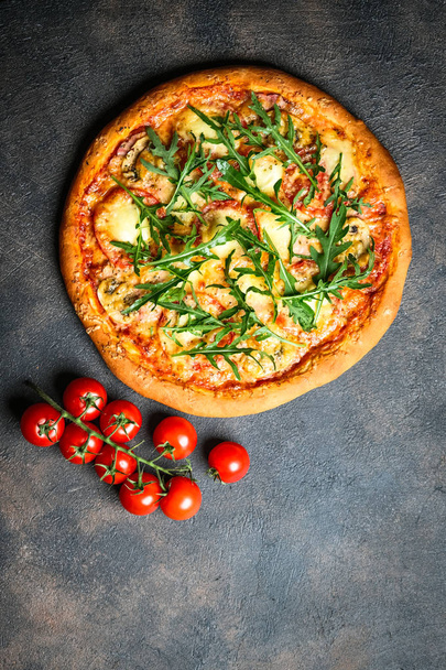 Tradycyjna włoska pizza z szynką, mozzarellą, bazylią, rukolą i pomidorami na ciemnym tle widok z góry przestrzeń kopia. - Zdjęcie, obraz