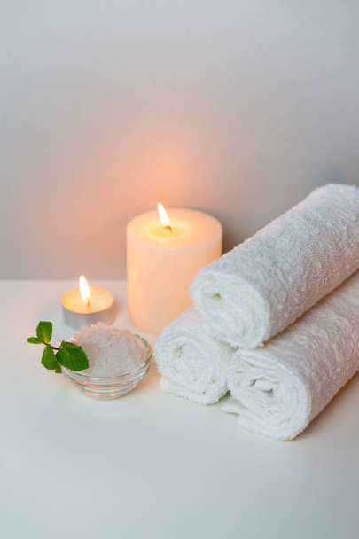 SPA procedure at salon vertical concept photo on grey background with stack of white towels, candles and cup of sea salt. - Φωτογραφία, εικόνα