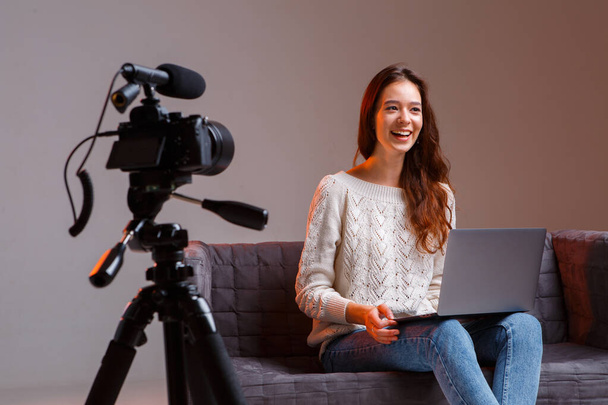 Young teen girl blogger makes a video stream on the couch at home. A video camera on a tripod and a laptop. - Фото, зображення