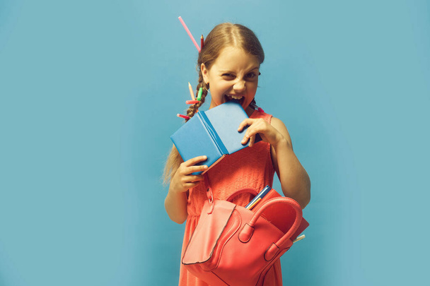 Girl with pink bag bites notebook. Kid with naughty face - Foto, Imagen