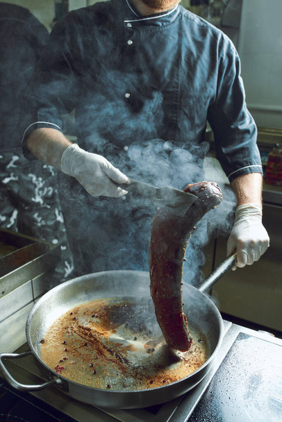 A séf az étterem konyhájában dolgozik. Nagy serpenyőben sült friss hús. Étterem konyha háttér - Fotó, kép