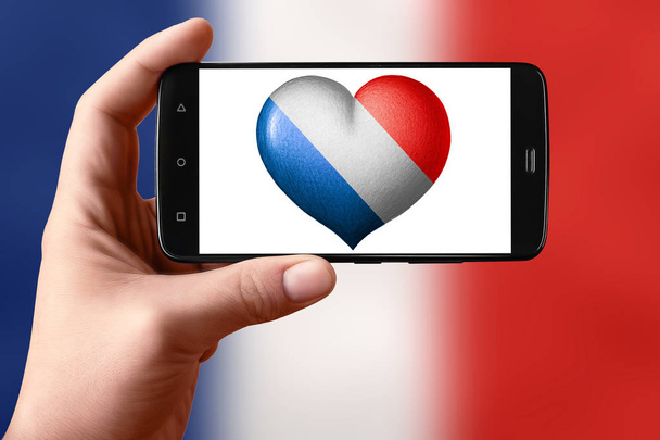 Bandeira da França em forma de coração na tela do telefone. Smartphone na mão mostra um coração de bandeira
.  - Foto, Imagem