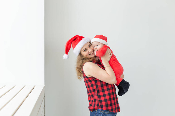 Family, childhood and Christmas concept - Young mother holding baby in santa suit indoor - Photo, Image