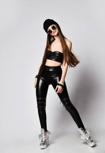Smiling relaxed woman in brutal wear tight leather leggings and round sunglasses is dancing swaying from side to side - Foto, Bild