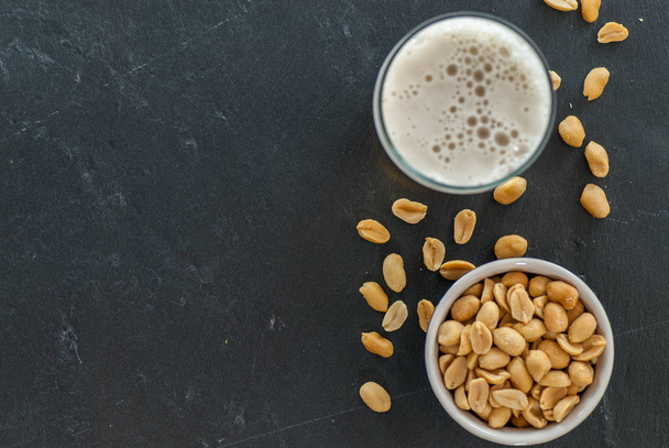 glass of beer and bowl with roasted and salted peanuts on slate social drinking concept - Foto, Imagen