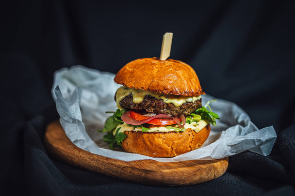 Domowej roboty hamburger wołowy z niebieskim serem i rukolą podawane na drewnianym talerzu na ciemnym tle  - Zdjęcie, obraz
