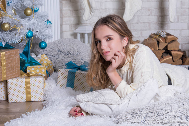 happy teenage girl sitting near christmas tree. Happy young lady with curlu hair gifts by the fireplace near the Christmas tree. New year concept. Xmas. - Fotografie, Obrázek