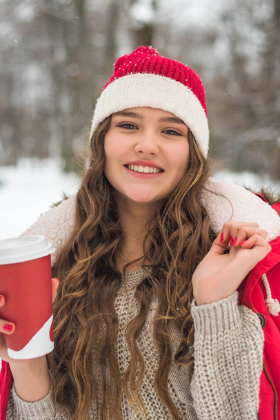 Piękny uśmiech cute nastolatek z naturalnym makijażu i długie włosy posiada filiżankę z gorącej kawy lub herbaty. Sezon zimowy. - Zdjęcie, obraz