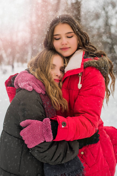 Kerstmis, Nieuwjaar, wintervakantie concept. Schattige tienermeisjes met krullend haar knuffelen en spelen met sneeuw in het park. - Foto, afbeelding