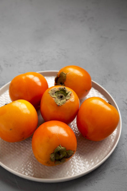 Raw Ripe Orange Persimmons on a plate over gray surface, low ang - Photo, Image