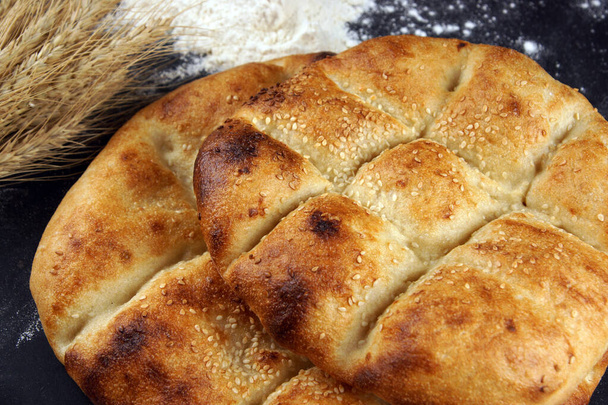 Two pita breads with a golden crust and sesame seeds lie on a table with flour - Photo, Image