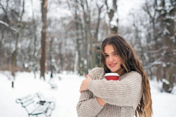 schöne lächelnde süße Teenager-Mädchen mit natürlichem Make-up und langen Haaren hält eine Tasse mit heißem Kaffee oder Tee. Wintersaison. - Foto, Bild