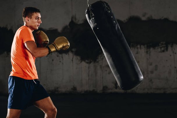 Ejercicio de boxeo de atleta joven en gimnasio de fitness sobre fondo oscuro. Concepto de boxeo de tiro duro de entrenamiento de hombre atlético.
 - Foto, imagen