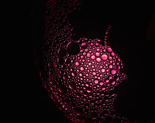 rode oliedruppels uit een mengsel van water en olijfolie verlicht met rood gekleurde bol - Foto, afbeelding