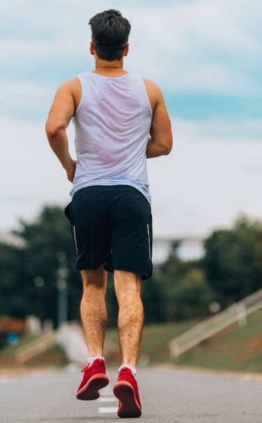 n atletische mannelijke oefening op een baan buiten tijdens het trainen joggen - Foto, afbeelding