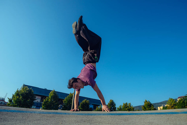 Sportman die zijn lichaam ondersteunt tijdens een handstand in het skateboard park van de stad - Foto, afbeelding