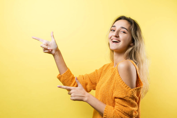 young beautiful woman with curly hair smiling and looking at camera pointing with finger and fingers to the side - Photo, Image