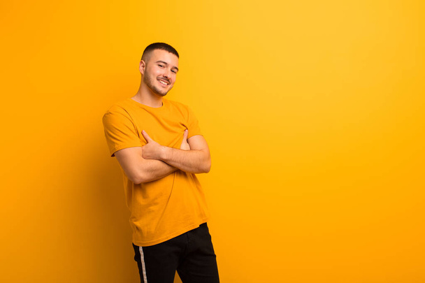 young handsome man laughing happily with arms crossed, with a relaxed, positive and satisfied pose against flat background - Photo, Image