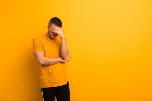 young handsome man looking stressed, ashamed or upset, with a headache, covering face with hand against flat background - Foto, imagen