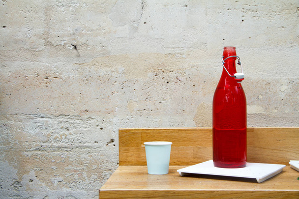 Zbliżenie butelki z czerwoną wodą i szkła na stole restauracyjnym do jasnej kamiennej ściany - Zdjęcie, obraz