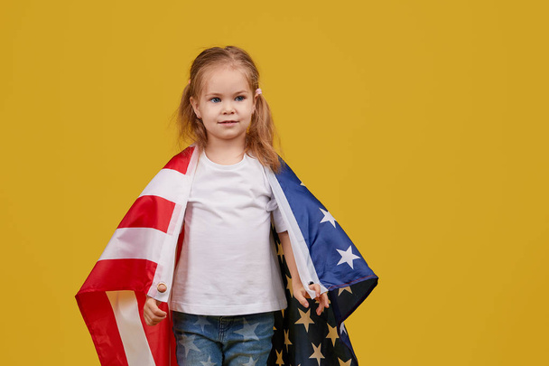 Férias patrióticas. Criança feliz, menina bonito com bandeira americana no fundo do estúdio amarelo. EUA celebram 4 de julho, Dia da Independência
. - Foto, Imagem