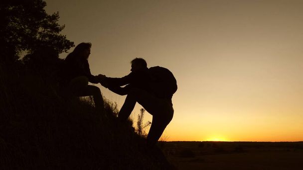 登山家のチームで働いています女性旅行者は丘の上に登るのを助ける男性旅行者の手を握っています。観光客の手を握って、日没で山に登る。ビジネスパートナーのチームワーク. - 写真・画像