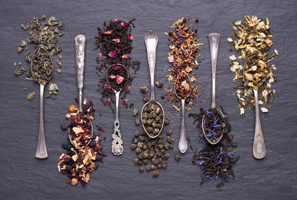 Assortment of dry green, black and fruit teas leaves in silver spoons on black stone background - Foto, Bild