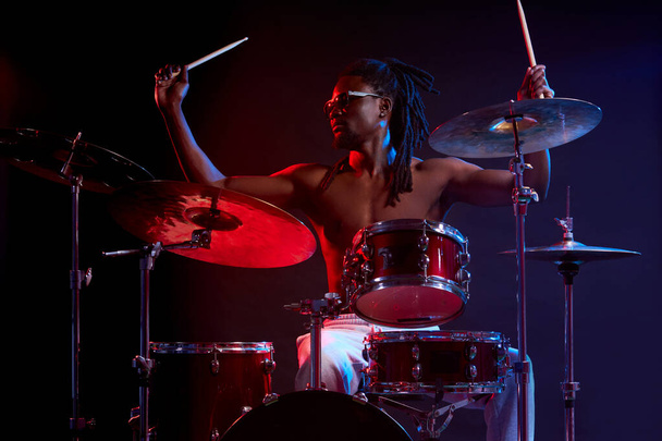 active african man playing on drums set in neon lights - Фото, зображення