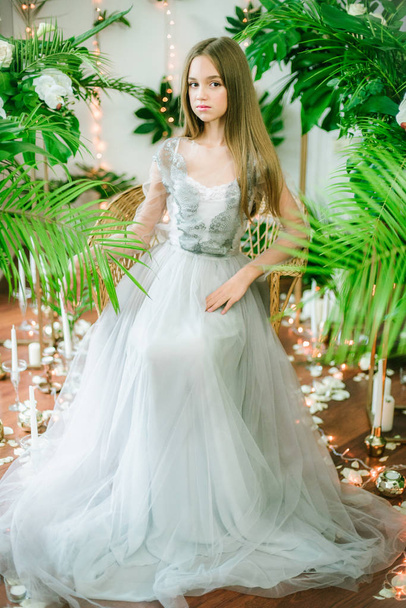 Attractive young girl with blond hair and evening make-up in a romantic dress among tropical greenery and white orchids, roses and lilies. Beauty and fashion - Фото, зображення