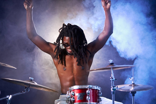 african man sit beating on drums in smoky space - Foto, afbeelding