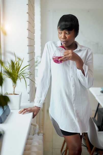 Charmant Afrikaans zakenvrouw drinken sap en kijken naar venster in modern kantoor - Foto, afbeelding