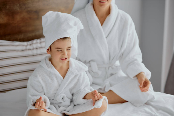beautiful mother and daughter sit in lotus pose on bed - Φωτογραφία, εικόνα