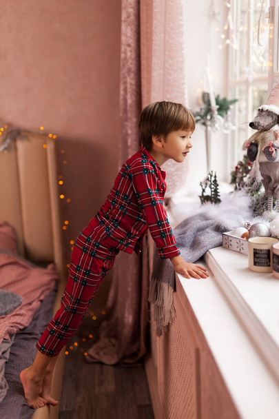 Liebenswerter Junge, der aus dem Fenster schaut und auf den Weihnachtsmann wartet - Foto, Bild