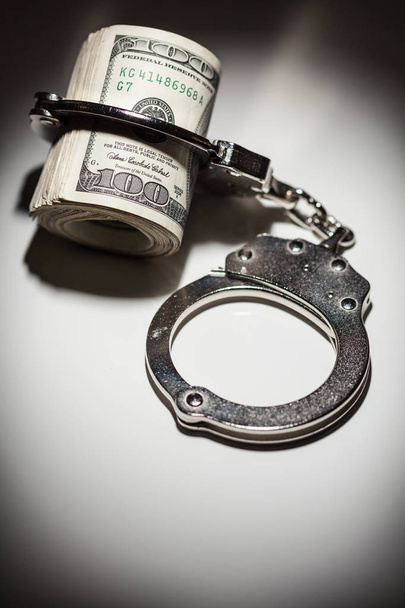 Handcuffs Locked on Roll of One Hundred Dollar Bills Under Spotlight - Foto, immagini