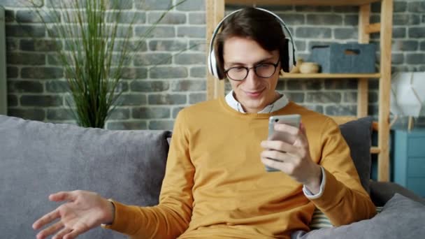 Slow motion of cheerful young man melomaniac enjoying music and using smartphone - Záběry, video