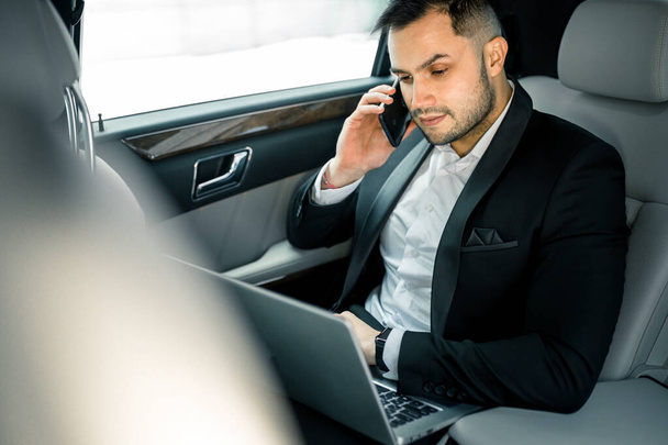personable confident man wearing tuxedo talking on phone in executive car - Foto, Imagen