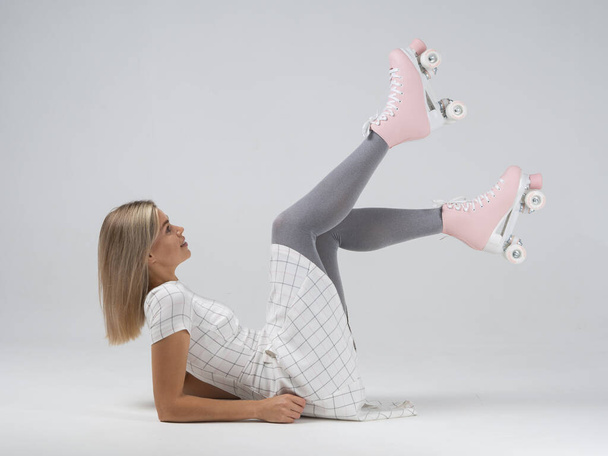 Blondes Mädchen in weißem Kleid und grauer Strumpfhose mit rosa Rollschuh Seitenansicht liegt mit hochgestellten Beinen - Foto, Bild