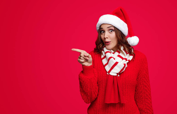 Surprised woman in Santa hat pointing aside - 写真・画像