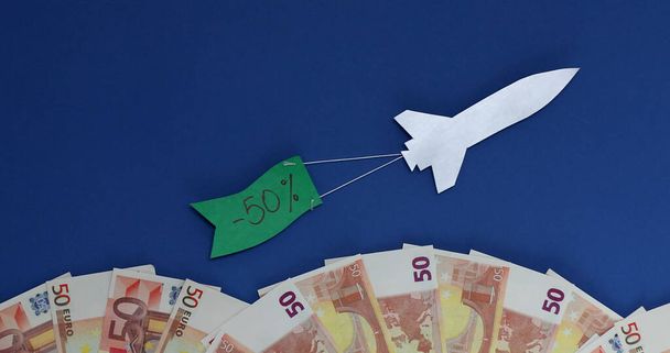 Un cohete vuela con una bandera con el descuento de texto menos 50 por ciento. olas de billetes en euros
. - Foto, Imagen