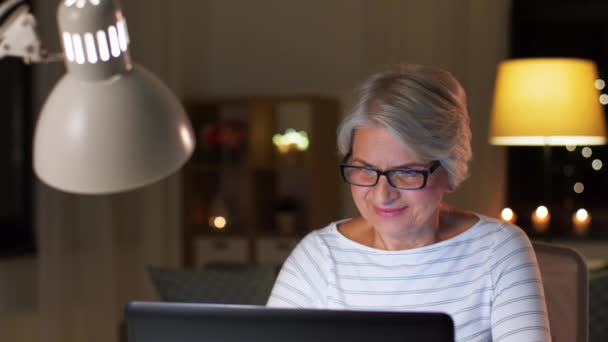 happy senior woman with laptop at home in evening - Imágenes, Vídeo