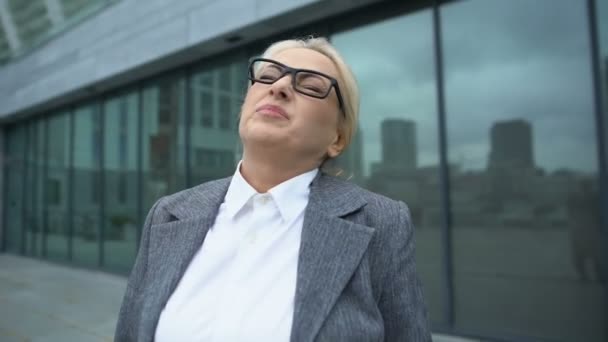 Mature female boss in eyeglasses turning head, suffering neck pain outdoor, ache - Materiał filmowy, wideo