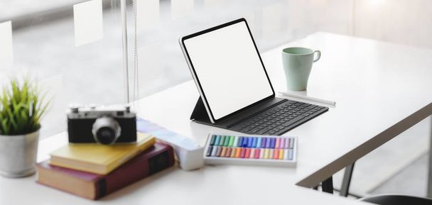 Oříznutý záběr moderního grafického pracoviště s prázdnou obrazovkou digitálního tabletu, fotoaparátu a kancelářských potřeb na bílém stole  - Fotografie, Obrázek