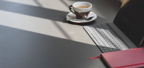 Moderní kancelářská místnost s digitálním tabletem a kancelářskými potřebami na tmavě šedém stole s kopírovacím prostorem a slunečním světlem  - Fotografie, Obrázek