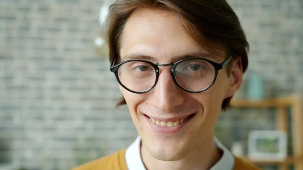 Close-up portrait of young man in trendy glasses smiling standing indoors in house - Filmati, video