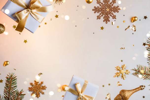 Καλά Χριστούγεννα και Πρωτοχρονιά. Χριστουγεννιάτικη κάρτα διακοπών φτιαγμένη από ιπτάμενες διακοσμήσεις, χρυσά κλαδιά ελάτης, μπάλες, νιφάδες χιονιού, λάμψη, κουτιά δώρων, bokeh, φως σε χρυσό φόντο. Επιλεκτική εστίαση - Φωτογραφία, εικόνα
