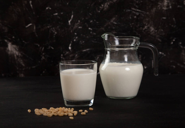 Vegetable milk from pine nuts in a glass and a glass jug on a black background.Horizontal - Foto, afbeelding