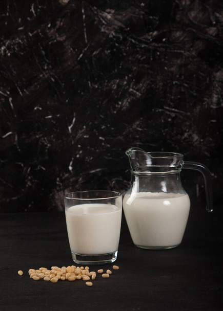 Vegetable milk from pine nuts in a glass and a glass jug on a black background. vertical - Foto, afbeelding