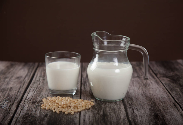 Vegetarian pine nut milk in a glass cup and jug on wooden background. Horizontally - Foto, afbeelding