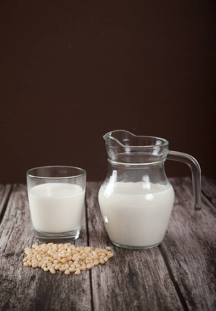 Vegetarian pine nut milk in a glass cup and jug on wooden background. vertical - Foto, afbeelding