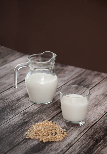 Vegetarische pijnboompitten melk in een glazen beker en kan op houten ondergrond. - Foto, afbeelding